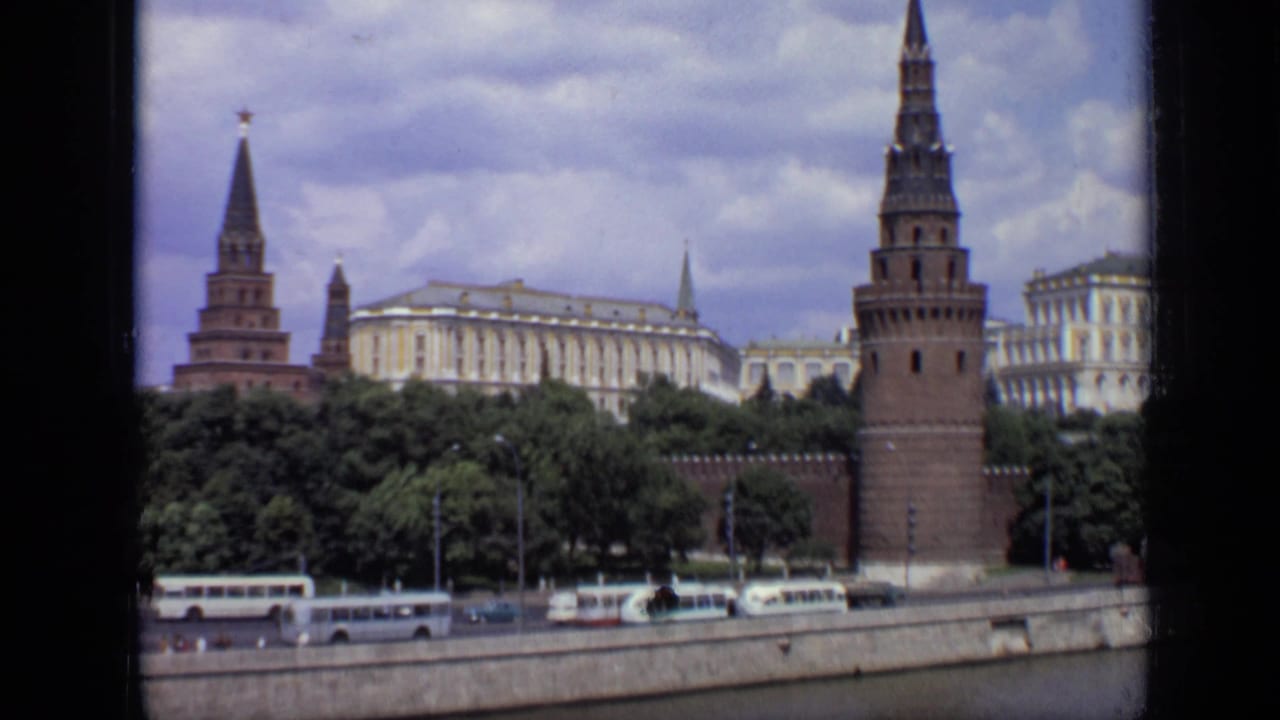 Kremlin towers and buildings above a river embankment with buses and cars.