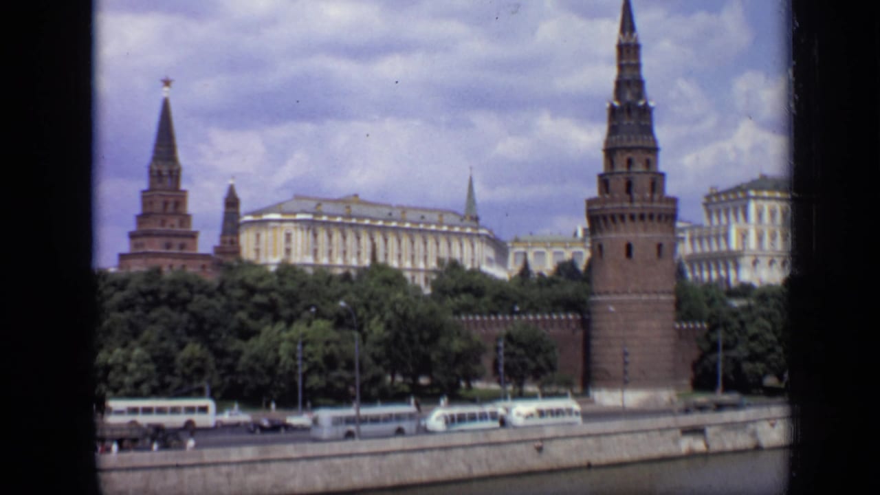 1971 Moscow view across the river toward Kremlin towers, pale buildings, trees, and small vehicles on the embankment road.