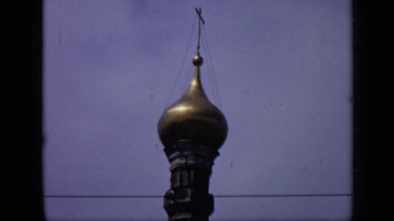 Gilded onion dome with cross against a blue sky and dark film borders.
