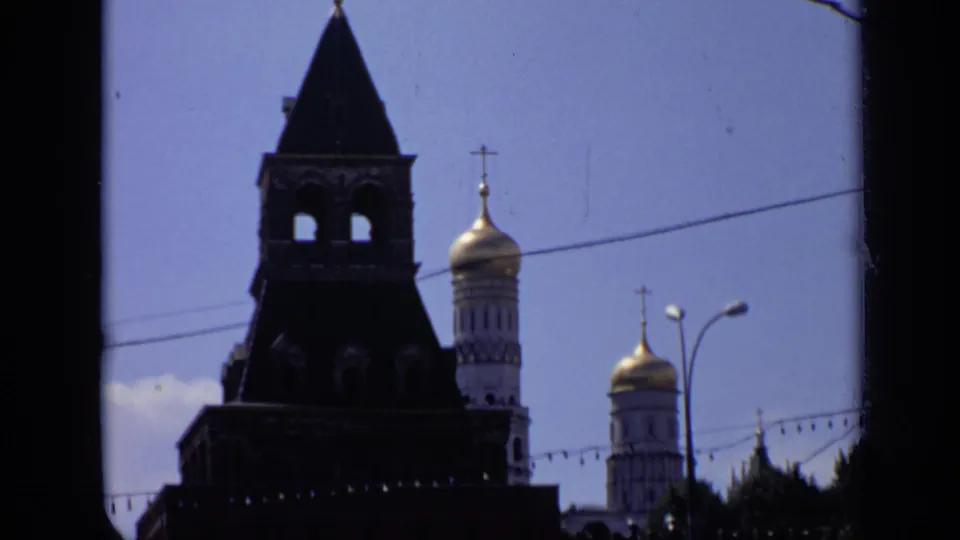 1971 Moscow 8mm view of a Kremlin tower, gilded domes with crosses, overhead wires, street lamps, and soft film contrast.