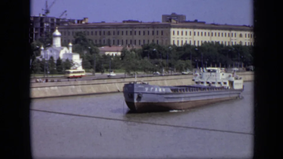 A cargo barge with Cyrillic lettering passes along the Moscow riverfront in 1971, with a church and large buildings behind the embankment.