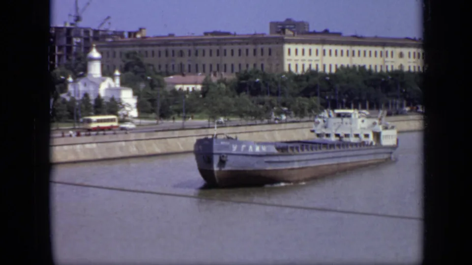 1971 Moscow view of a barge moving past the embankment, with a domed church, traffic, trees, cranes, and Soviet-era buildings in the background.