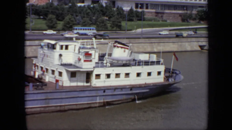 Moscow, 1971: a white riverboat with deck structures moves along the river beneath a road with cars and a blue bus.