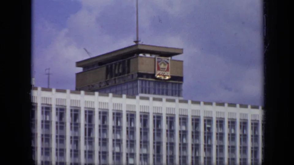 1971 Moscow street view with a red-and-white Sovtransavto bus, parking sign, and white building topped by a Soviet-era emblem.