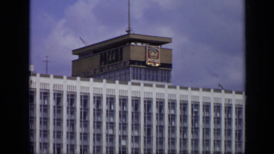 1971 Moscow view of the Sovtransavto bus beneath a white modernist building, with a rooftop emblem and clear sky visible.