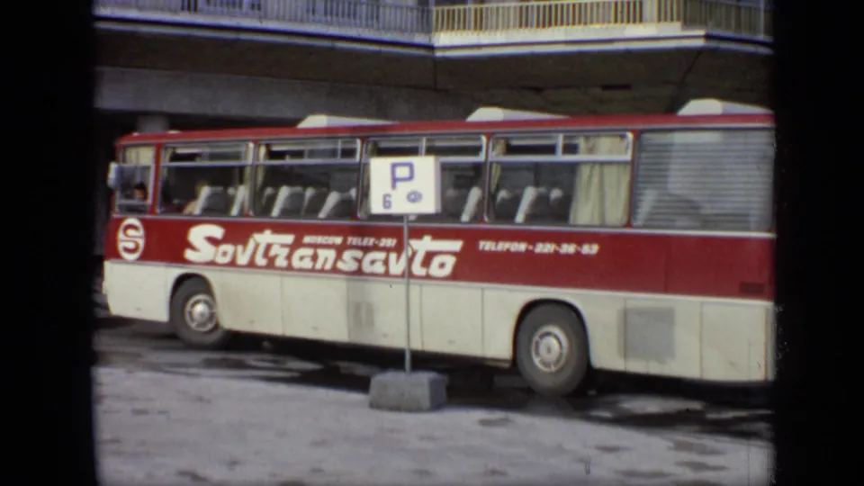1971 Moscow frame with the Sovtransavto bus filling the foreground and the white building and rooftop emblem behind it.