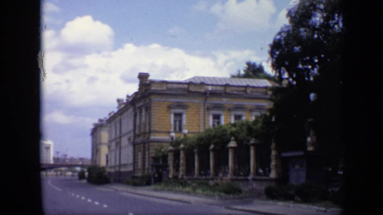 Yellow classical building beside a quiet road under a cloudy summer sky.