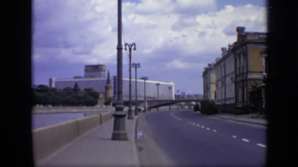 1971 Moscow street scene showing a broad riverside roadway, tall lampposts, distant Soviet-era block architecture, and a classical facade.