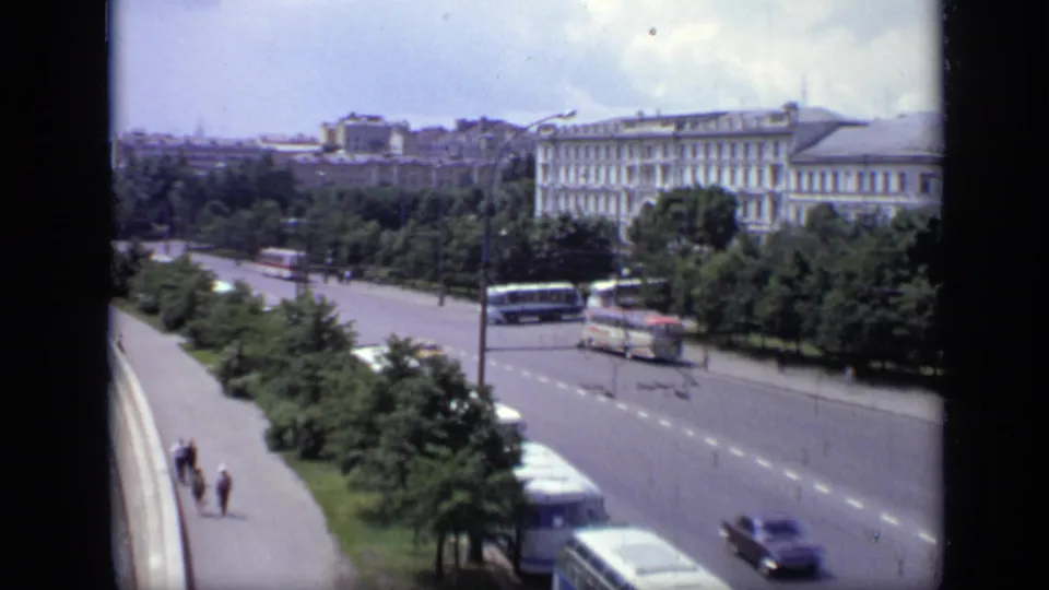 Elevated 1971 Moscow view with buses and cars on a broad road, pedestrians on the sidewalk, trees, and a large pale building.