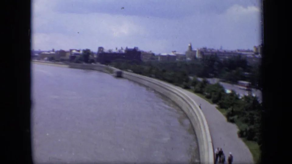 End of the 1971 Moscow pan showing the broad river, sweeping embankment, small pedestrian group, roadside trees, and distant buildings.