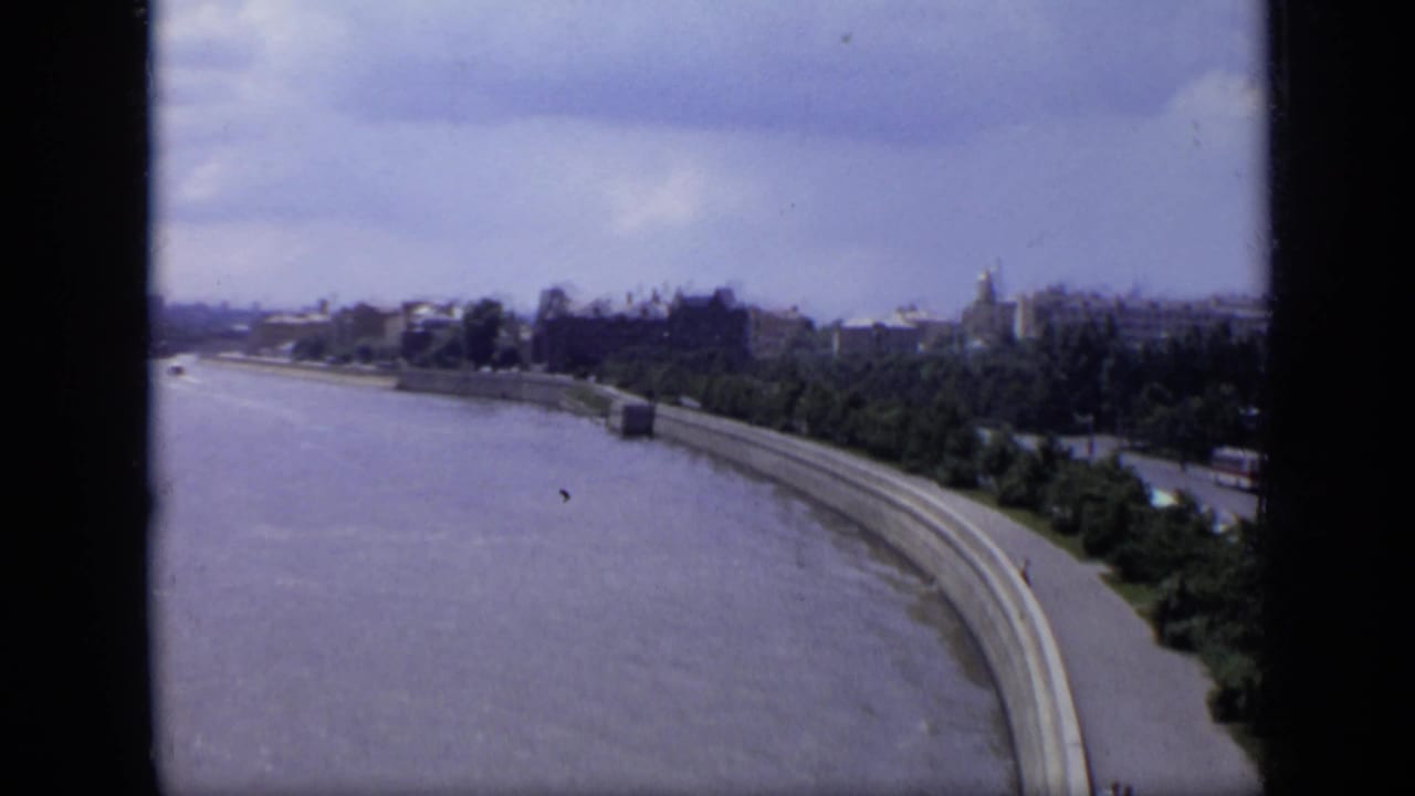 1971 8mm view over Moscow with the river bend, concrete embankment, trees, and distant city skyline under a cloudy sky.