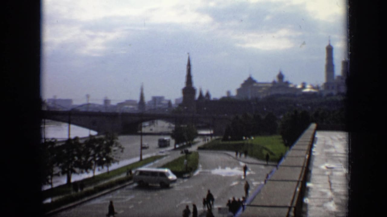 1971 Moscow home-movie frame showing a river bridge, distant towers and domes, a white van, and pedestrians along the embankment.
