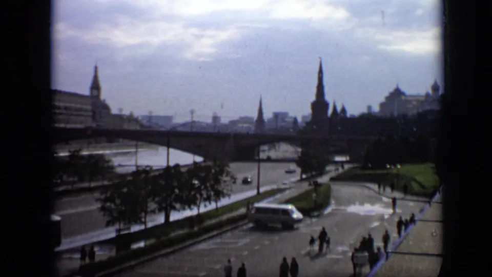 1971 Moscow 8mm frame showing bridge arches over the river, distant landmark towers, roadside trees, cars, and pedestrians.