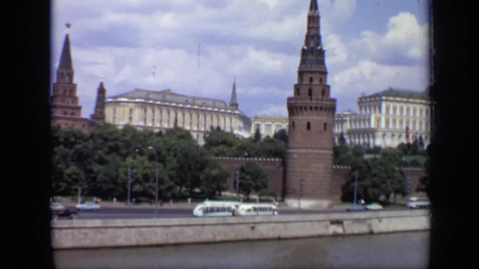 1971 Moscow view across the river toward a Kremlin tower and wall, with buses and cars moving along the embankment below.