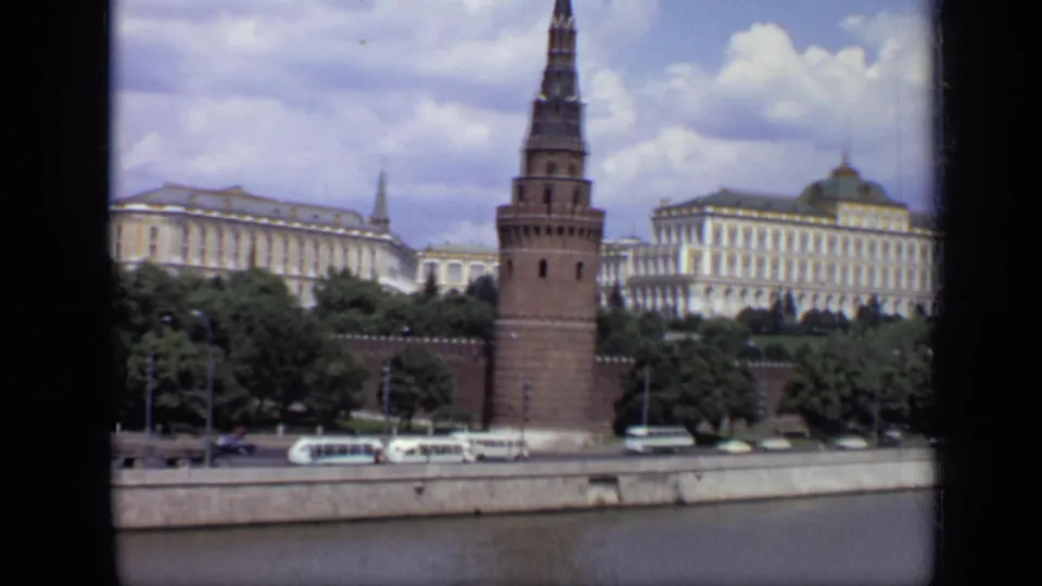 Final 1971 Moscow frame showing the Kremlin tower and wall beside a domed building, with riverfront buses and cars in the foreground.
