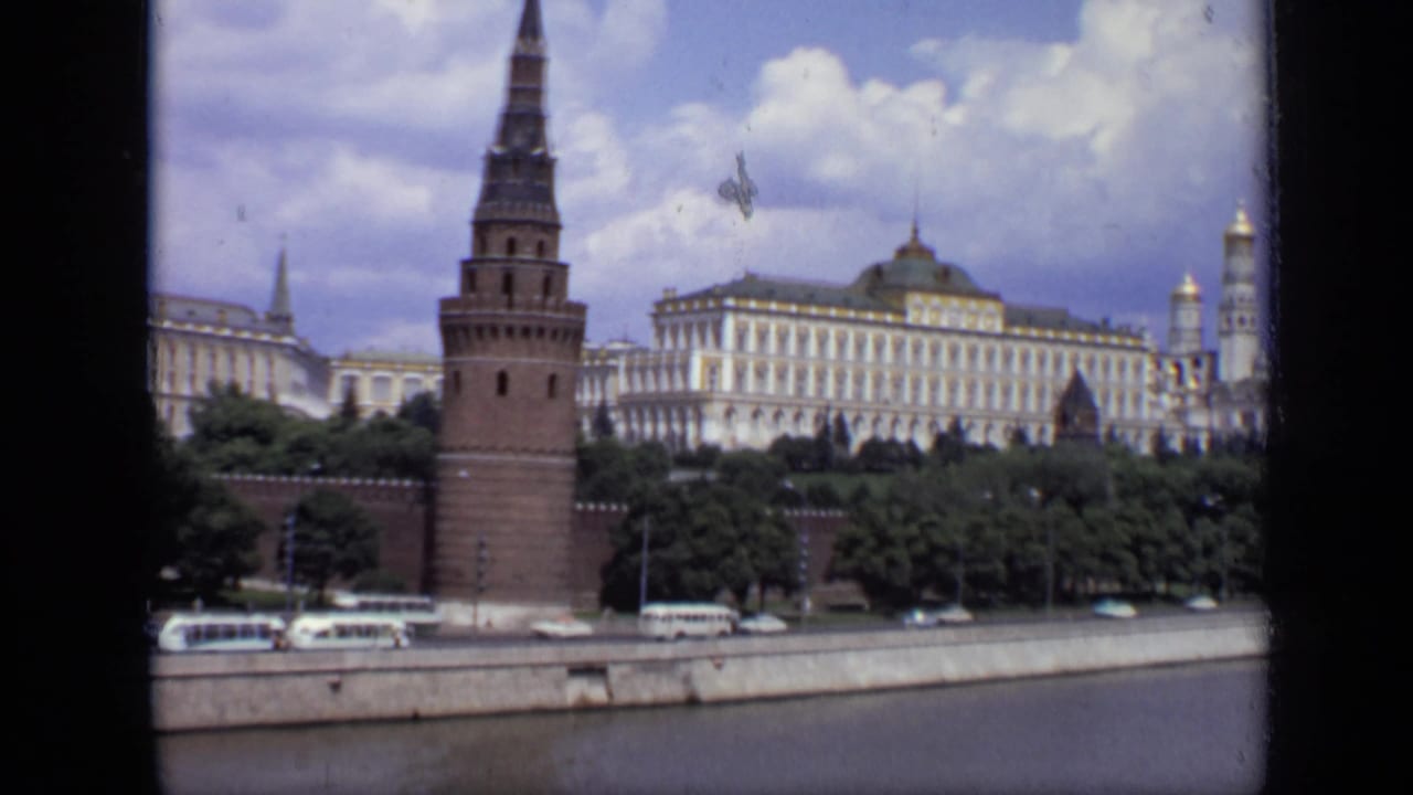 Kremlin tower and white buildings behind trees, with buses and cars on the embankment road.