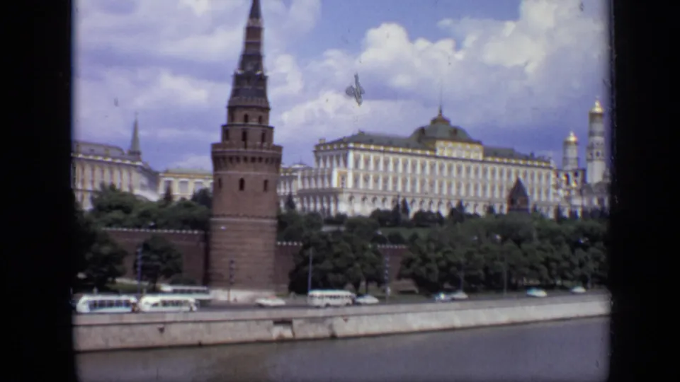 1971 Moscow frame showing the Kremlin tower and pale buildings above trees, with Soviet-era road traffic near the river.