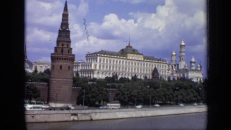 1971 Moscow view with a red-brick Kremlin tower at left, palace buildings and domes behind, trees, buses, and riverside roadway.