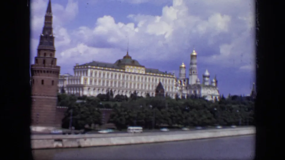 1971 Moscow riverside frame showing the Kremlin tower and long pale building behind trees, with domes and traffic along the embankment.