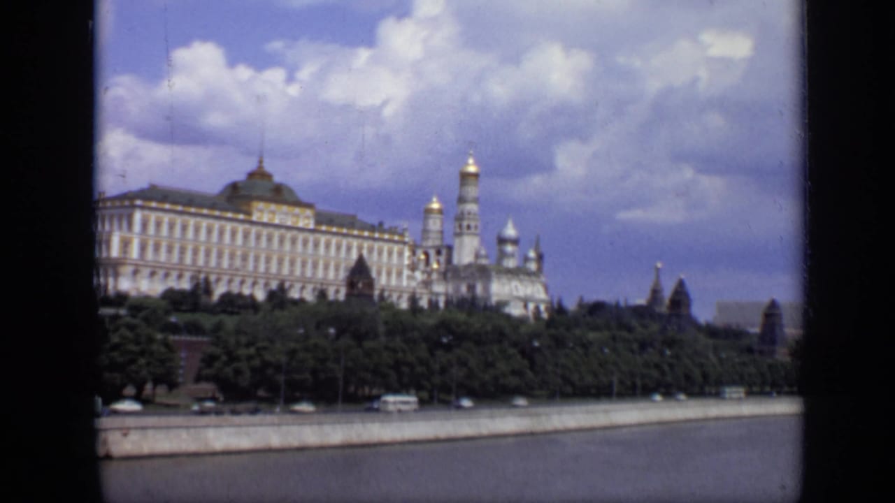 Wide riverfront view of Kremlin architecture, trees, clouds, and traffic.
