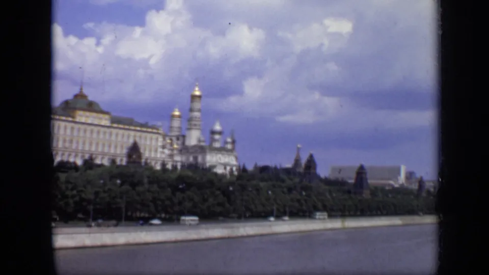1971 8mm frame with the Kremlin partly cropped at left, church towers near center, trees, buses, river, and a cloudy sky.