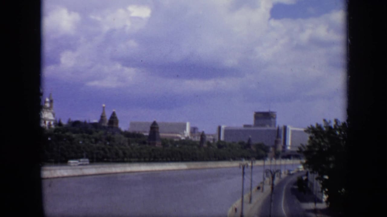 1971 Moscow pan along the Moskva River with historic Kremlin forms, modern blocks, trees, and a curving riverside embankment.