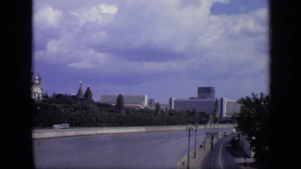 1971 Moscow pan along the Moskva River with historic Kremlin forms, modern blocks, trees, and a curving riverside embankment.