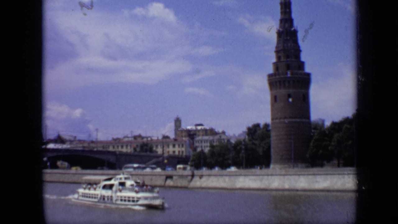1971 Moscow 8mm frame showing a white sightseeing boat moving along the river below a Kremlin tower and distant city buildings.