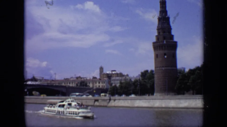1971 Moscow 8mm frame showing a white sightseeing boat moving along the river below a Kremlin tower and distant city buildings.