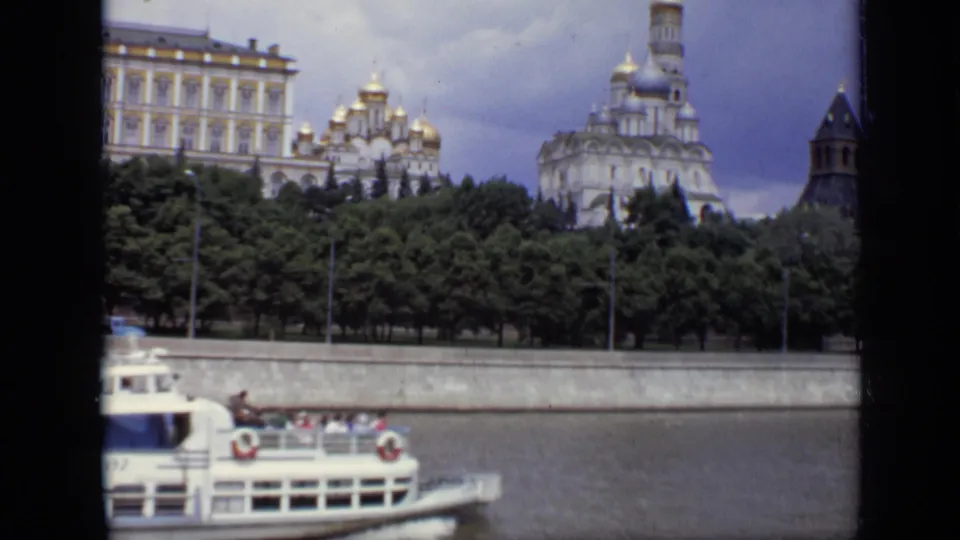 1971 Moscow frame with Kremlin walls, domed church architecture, trees, riverfront, and the edge of a passing passenger boat.