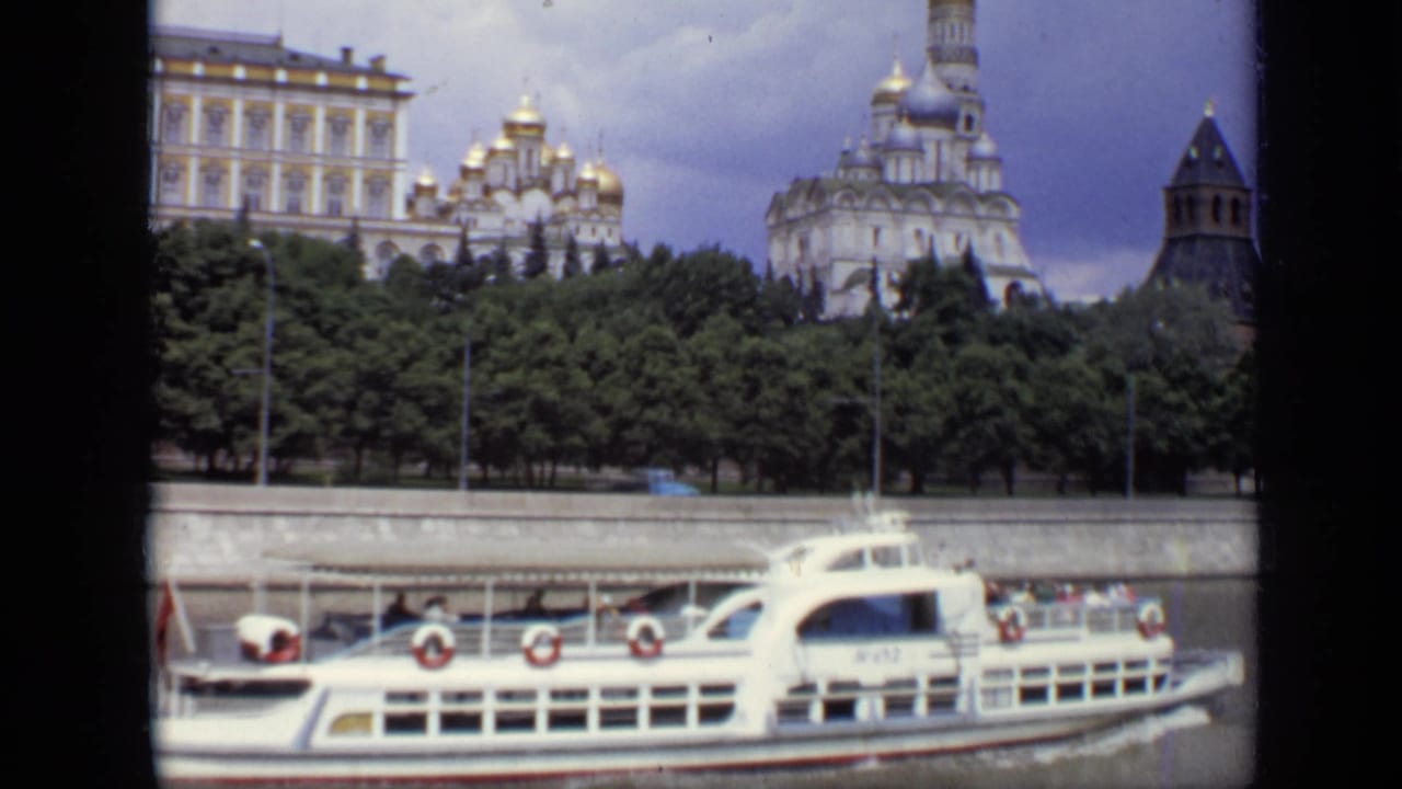 White tourist boat on the Moscow River with Kremlin buildings and trees behind it.
