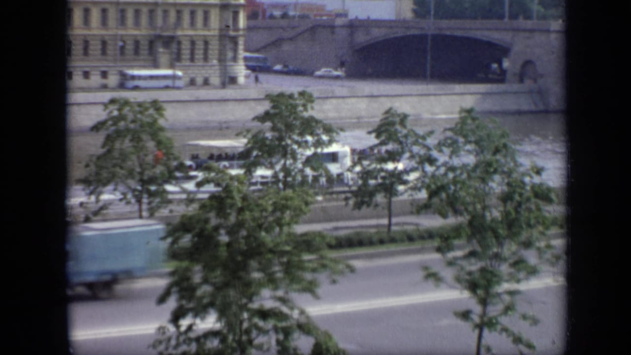 1971 Moscow riverfront seen from above, with cars on an embankment road, trees, a stone bridge, and riverside buildings.