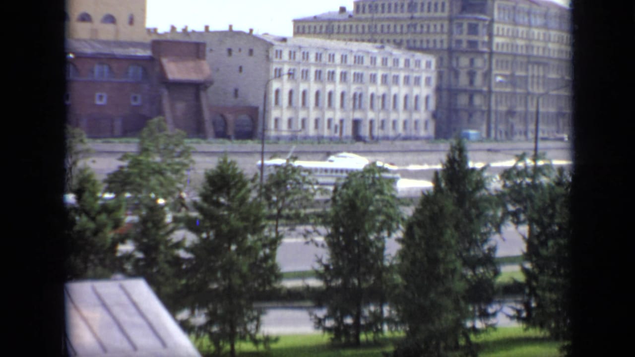 1971 Moscow 8mm view from behind a dark frame toward trees, embankment road, and multi-story buildings.