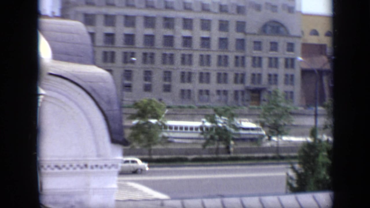 Riverside road and building seen past white domes and dark vertical foreground bars.