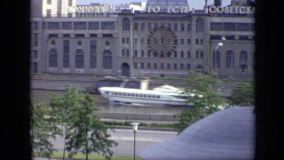 1971 Moscow riverside frame showing a white passenger boat on the water, trees, road lanes, and a large building with Cyrillic signage.