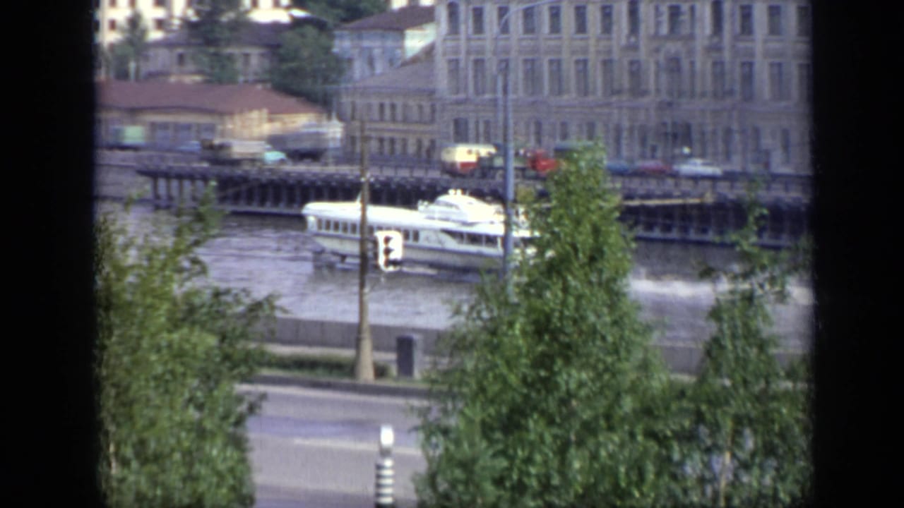 White riverboat passing an urban embankment seen through a dark window frame.