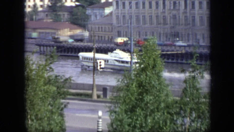 1971 Moscow home-movie view of a white riverboat moving along a broad waterway past buildings and trees, partly framed by a window.