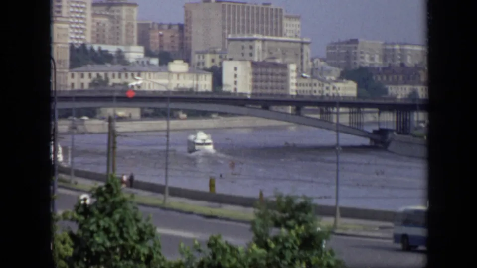 Elevated 1971 Moscow view of a riverboat below a bridge, with apartment blocks, embankment traffic, trees, and a blue bus in the frame.