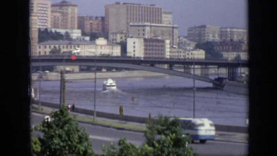 1971 8mm view over a Moscow riverfront, showing a bridge, embankment road, moving traffic, trees, and Soviet-era buildings.