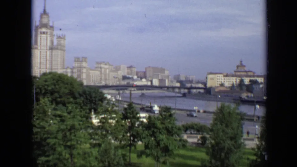 Wide 1971 Moscow view showing a tall skyline building, river bridge, embankment traffic, trees, and distant apartment blocks.