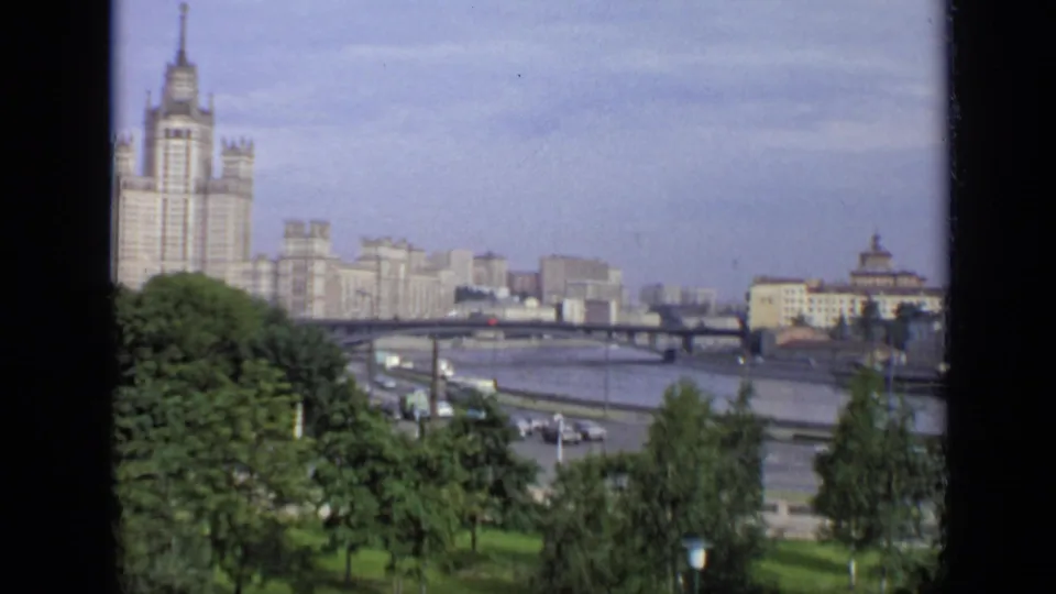 1971 Moscow frame with leafy foreground trees, a broad river, bridge traffic, and pale Soviet-era buildings beyond.