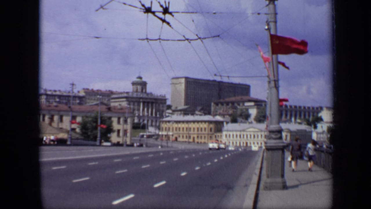 Wide Moscow avenue with trolley wires, red flags, cars, pedestrians, and large buildings.