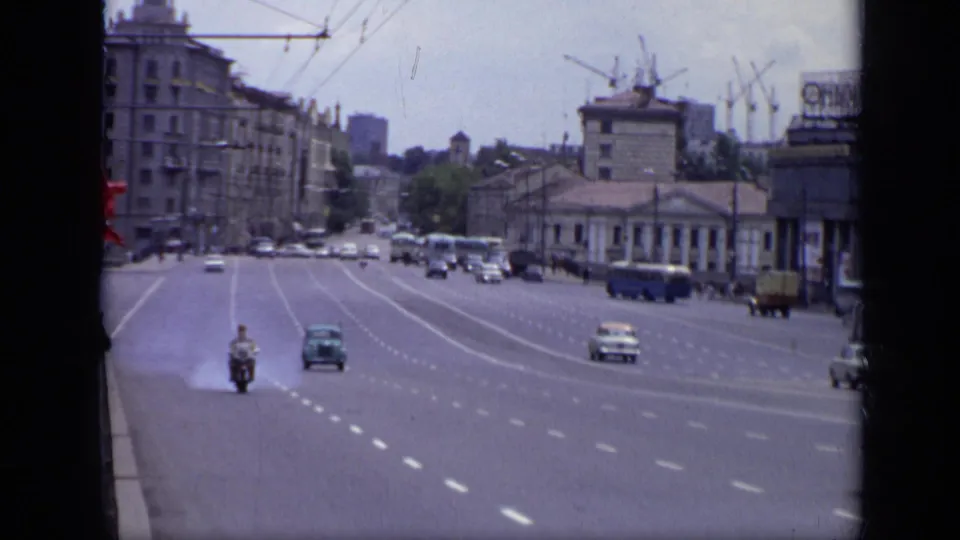 1971 Moscow avenue scene with oncoming cars, a motorcycle, buses, distant pedestrians, large buildings, and cranes on the skyline.