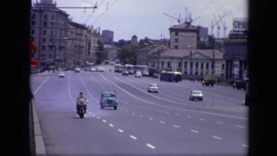 1971 Moscow traffic view showing a motorcycle and cars approaching on a wide avenue, with buses, pedestrians, buildings, and cranes beyond.