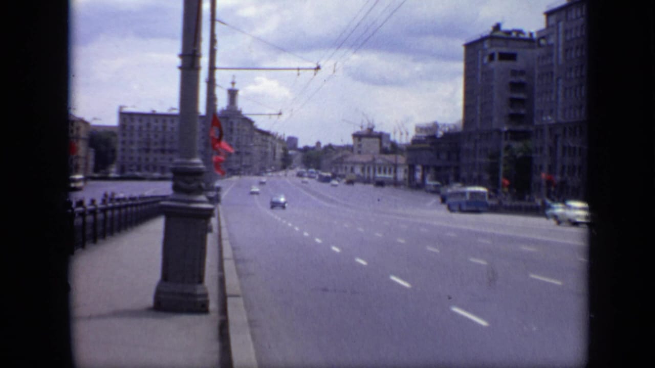 1971 Moscow avenue viewed from a bridge or sidewalk, with light traffic, red flags, overhead wires, and Soviet-era buildings.