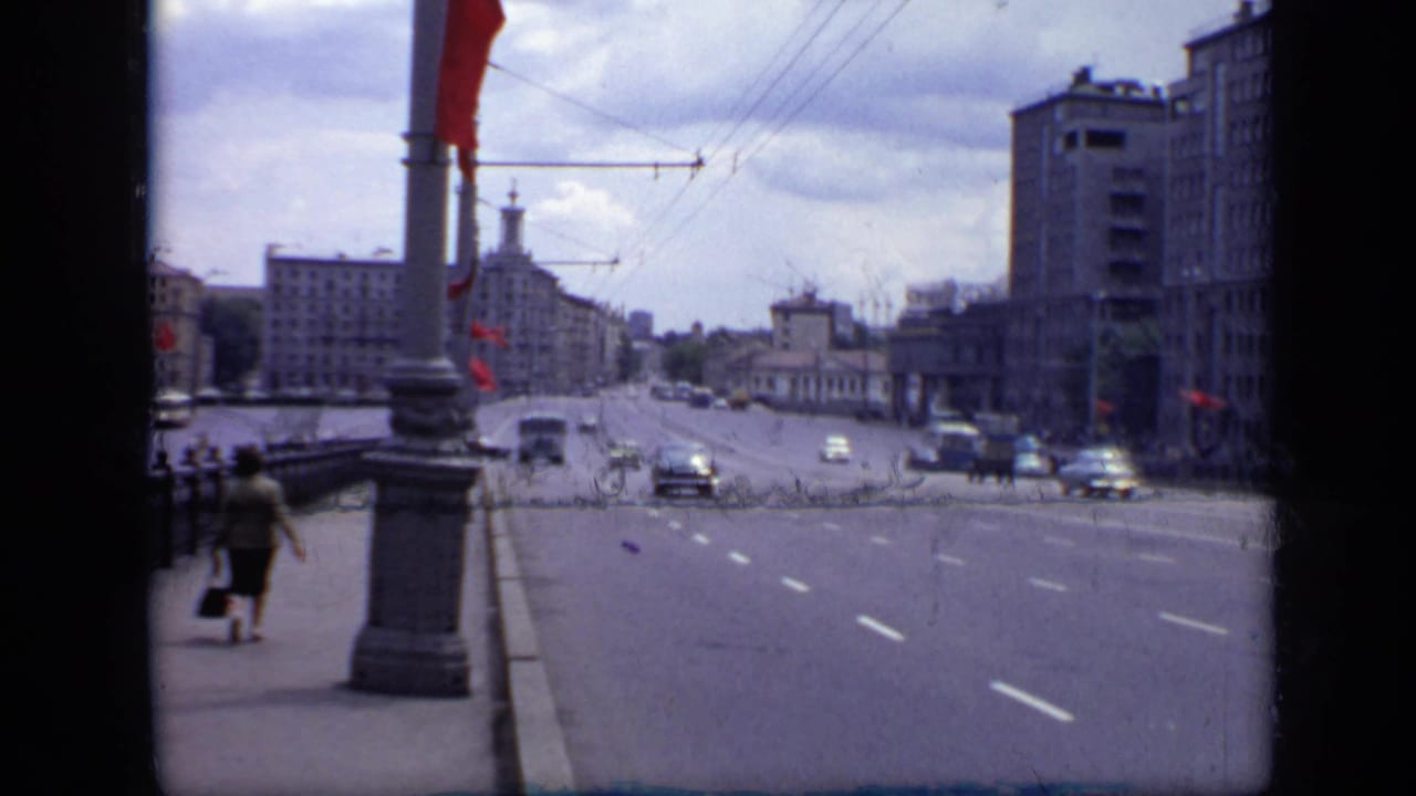 1971 Moscow 8mm view across a broad street with pedestrians on the sidewalk, red flags on poles, period cars, and large urban buildings.