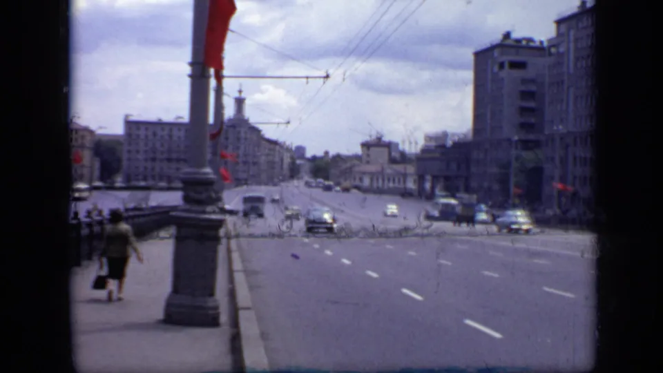 1971 Moscow 8mm view across a broad street with pedestrians on the sidewalk, red flags on poles, period cars, and large urban buildings.
