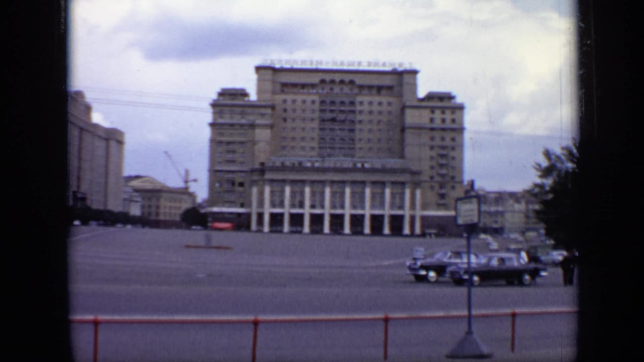 Large Soviet-era building with columns and Cyrillic rooftop signage beside a wide open roadway.