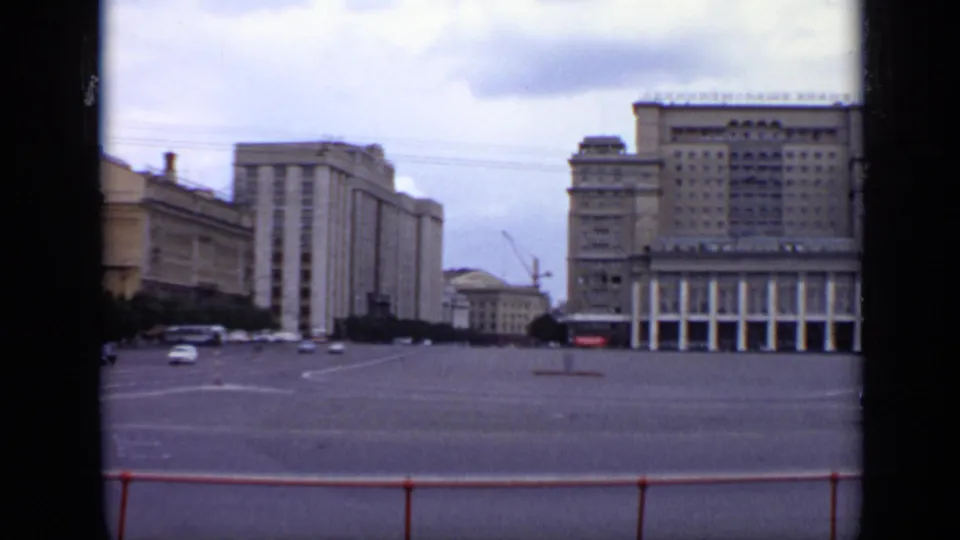 1971 Moscow 8mm view across an open roadway toward large Soviet-era buildings, with a few period cars and Cyrillic signage visible.