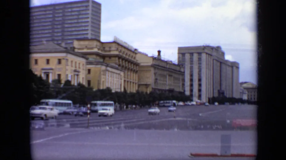 1971 Moscow home-movie frame of traffic moving through a wide urban square bordered by monumental buildings and tall housing blocks.